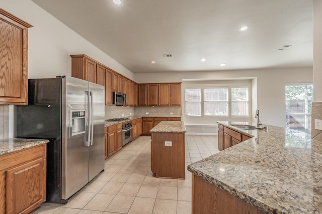 kitchen with sink, light stone counters, appliances with stainless steel finishes, tasteful backsplash, and an island with sink