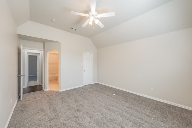 unfurnished bedroom with a closet, connected bathroom, vaulted ceiling, light colored carpet, and ceiling fan