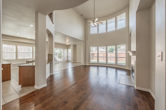 unfurnished living room with hardwood / wood-style floors, a towering ceiling, and ceiling fan