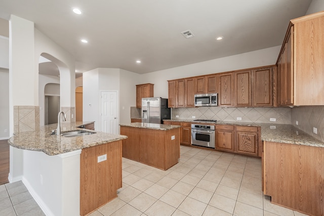 kitchen with kitchen peninsula, appliances with stainless steel finishes, sink, and light stone countertops