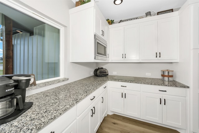 kitchen featuring white cabinetry, stainless steel microwave, light hardwood / wood-style floors, and light stone countertops