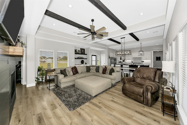 living room with beamed ceiling, light hardwood / wood-style floors, and ceiling fan with notable chandelier