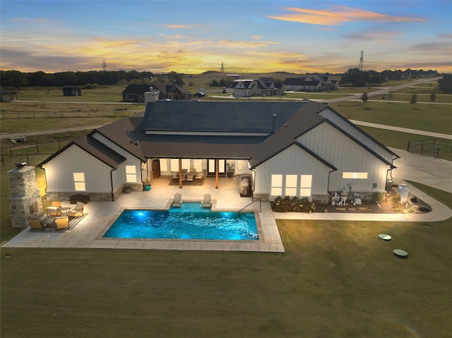 back house at dusk with a yard, a patio, and a swimming pool with hot tub