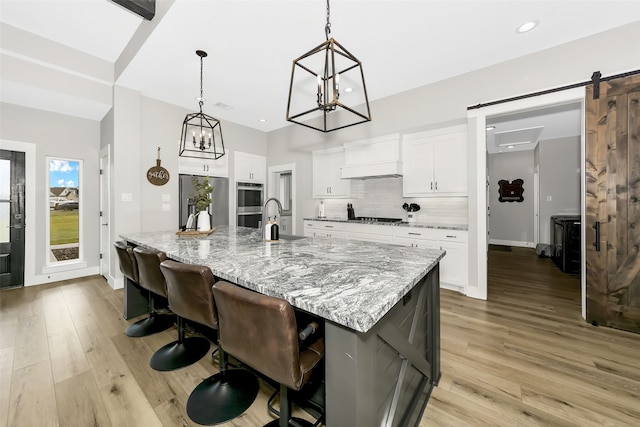 kitchen with decorative light fixtures, a barn door, light stone countertops, light hardwood / wood-style floors, and white cabinets