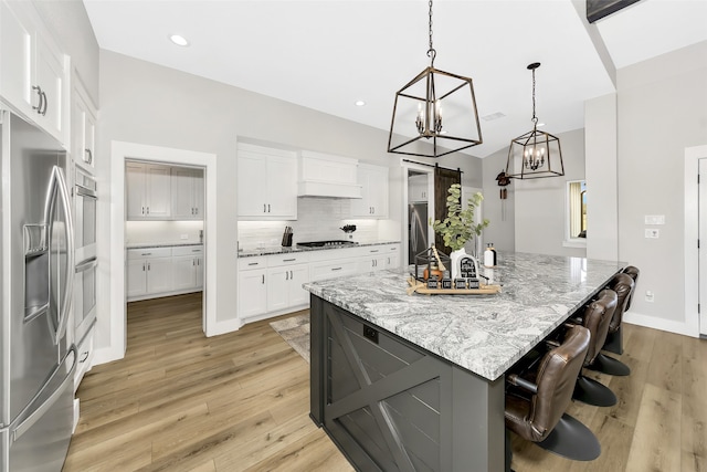 kitchen with white cabinetry, decorative light fixtures, a large island, light stone countertops, and stainless steel refrigerator with ice dispenser