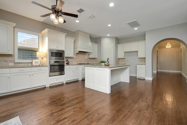 kitchen with stainless steel appliances, white cabinets, light stone counters, and a center island