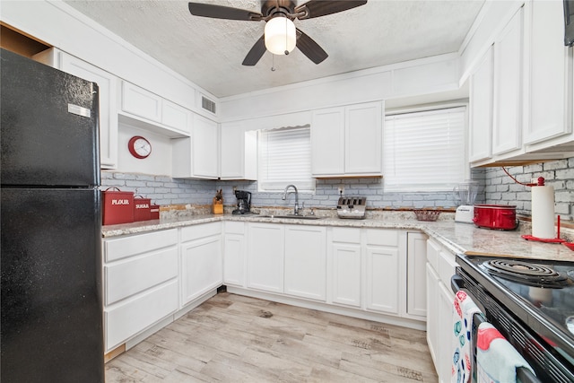 kitchen with white cabinetry, black fridge, light stone counters, and light wood-type flooring