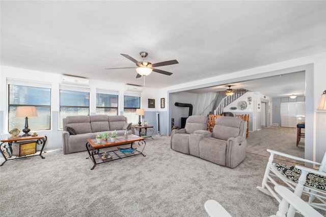 living room with a wall unit AC, a wood stove, ceiling fan, and light colored carpet