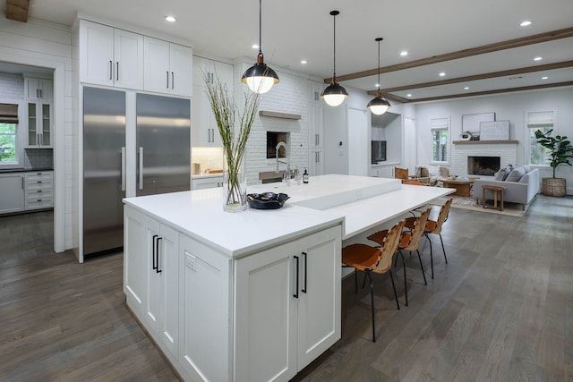 kitchen with built in fridge, white cabinets, decorative backsplash, an island with sink, and a fireplace