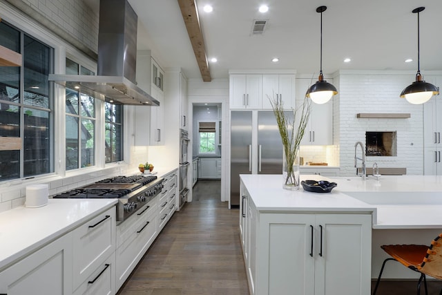 kitchen with stainless steel appliances, wall chimney exhaust hood, hanging light fixtures, and beam ceiling