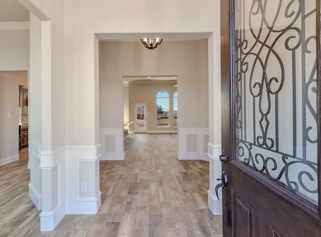 foyer with an inviting chandelier, ornamental molding, and light hardwood / wood-style flooring