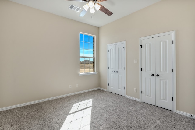 unfurnished bedroom featuring multiple closets, light carpet, and ceiling fan