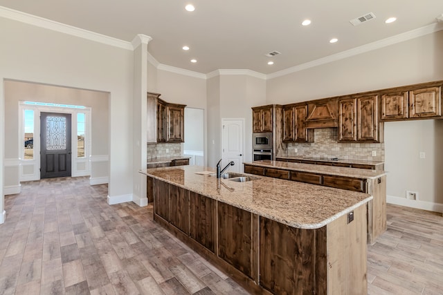 kitchen featuring light wood-type flooring, decorative backsplash, a center island with sink, and light stone countertops