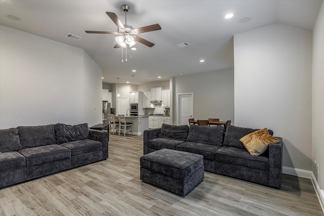 living room with light hardwood / wood-style flooring, ceiling fan, and vaulted ceiling