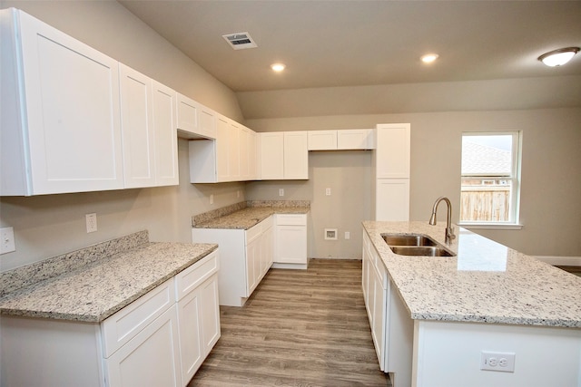 kitchen featuring white cabinetry, light stone countertops, sink, light hardwood / wood-style floors, and a kitchen island with sink