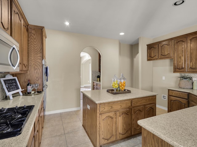 kitchen with black gas stovetop, light stone counters, light tile patterned floors, and a center island