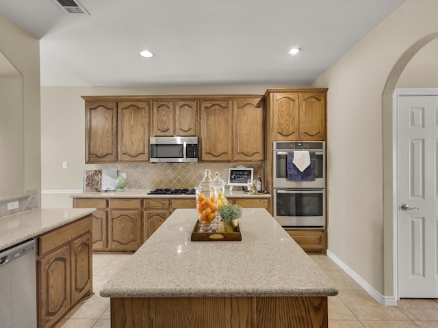 kitchen featuring a kitchen island, light stone countertops, appliances with stainless steel finishes, and light tile patterned floors