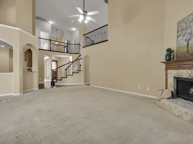 unfurnished living room featuring a fireplace, a towering ceiling, ceiling fan, and carpet flooring