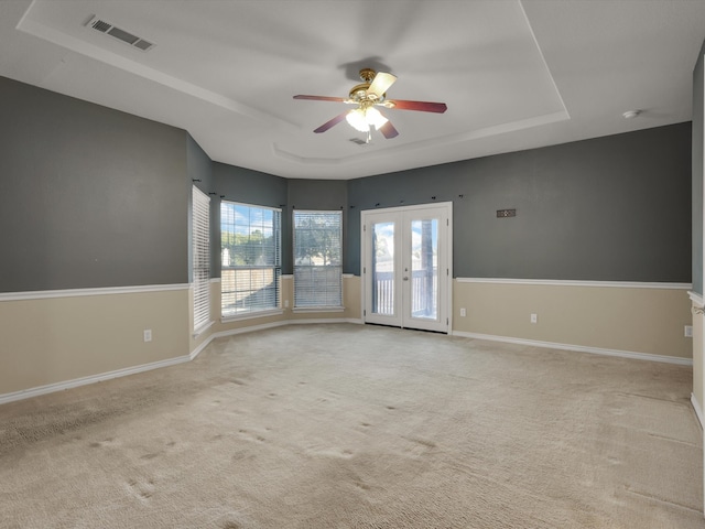 spare room with a tray ceiling, french doors, light colored carpet, and ceiling fan