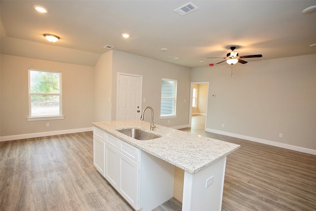 kitchen with white cabinetry, sink, light stone countertops, an island with sink, and light hardwood / wood-style flooring