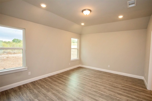 spare room with lofted ceiling, hardwood / wood-style flooring, and a healthy amount of sunlight