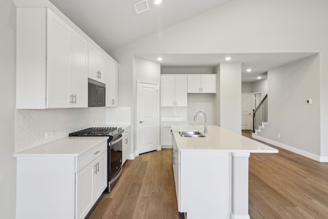 kitchen featuring white cabinetry, stainless steel gas range oven, an island with sink, backsplash, and sink