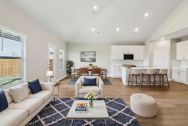 living room featuring high vaulted ceiling, sink, a wealth of natural light, and light wood-type flooring