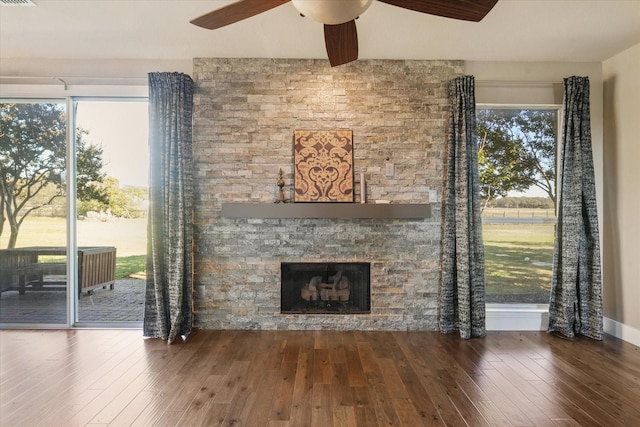 unfurnished living room with dark hardwood / wood-style floors, ceiling fan, and a stone fireplace