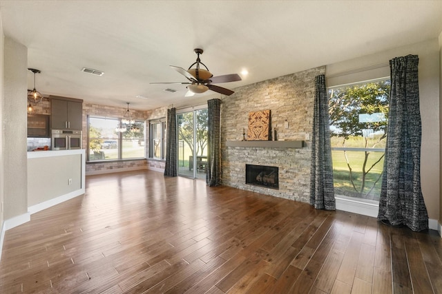 unfurnished living room featuring plenty of natural light, ceiling fan, dark hardwood / wood-style flooring, and a fireplace