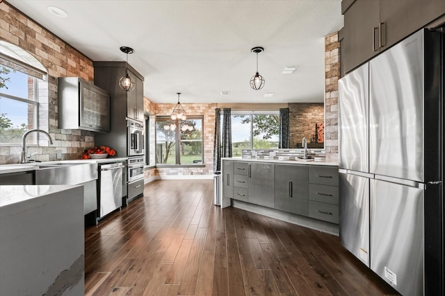 kitchen with dark hardwood / wood-style flooring, brick wall, decorative light fixtures, gray cabinets, and appliances with stainless steel finishes