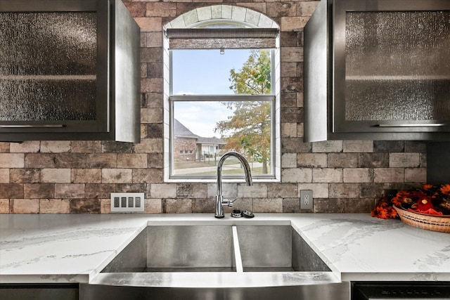 kitchen featuring light stone counters, black dishwasher, sink, and backsplash