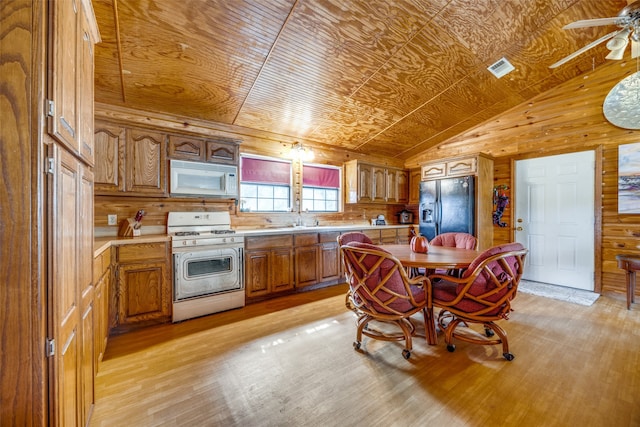 kitchen with wood walls, white appliances, light hardwood / wood-style flooring, and vaulted ceiling