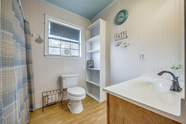 bathroom featuring wood-type flooring, toilet, wooden walls, ornamental molding, and vanity