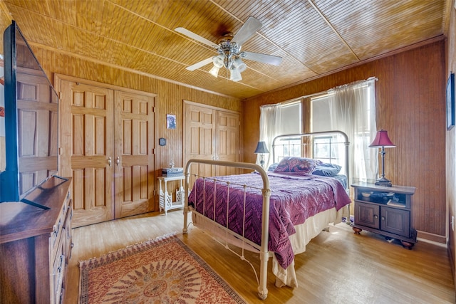 bedroom with light wood-type flooring, wooden walls, wooden ceiling, and ceiling fan