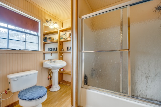 bathroom featuring wood walls, wooden ceiling, combined bath / shower with glass door, wood-type flooring, and toilet