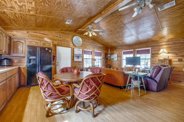 dining area with wood walls, vaulted ceiling with beams, ceiling fan, and light hardwood / wood-style flooring