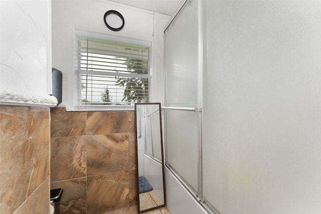 bathroom with tile walls and bath / shower combo with glass door