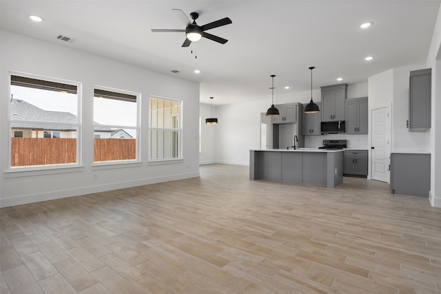 kitchen with light hardwood / wood-style flooring, an island with sink, gray cabinets, appliances with stainless steel finishes, and decorative light fixtures