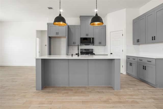 kitchen featuring gray cabinetry, a center island with sink, stainless steel appliances, backsplash, and sink