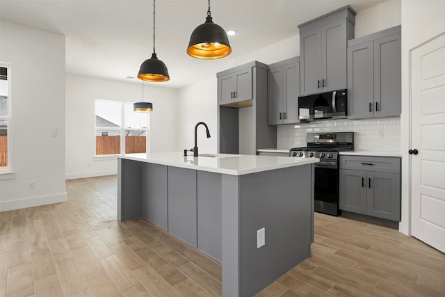 kitchen featuring gray cabinets, appliances with stainless steel finishes, a kitchen island with sink, and hanging light fixtures