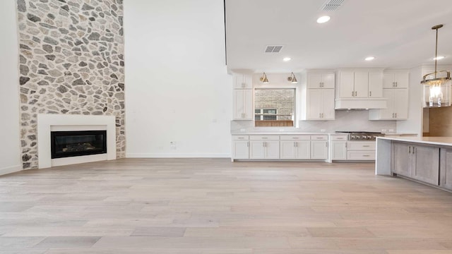 kitchen featuring light wood-type flooring, pendant lighting, under cabinet range hood, backsplash, and light countertops