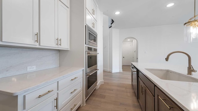 kitchen with light wood-type flooring, decorative backsplash, arched walkways, stainless steel appliances, and a sink