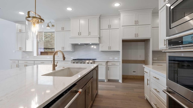 kitchen featuring white cabinets, stainless steel appliances, premium range hood, and a sink