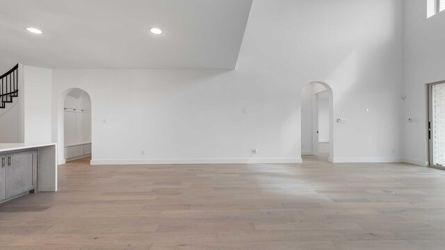 unfurnished living room featuring light wood-type flooring, arched walkways, and stairs