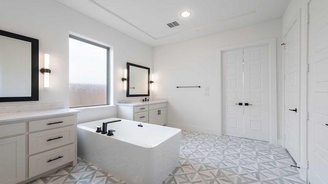 full bath featuring two vanities, recessed lighting, a freestanding tub, tile patterned floors, and a sink