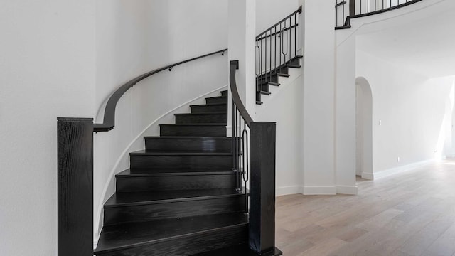 stairway with baseboards, arched walkways, wood finished floors, and a towering ceiling