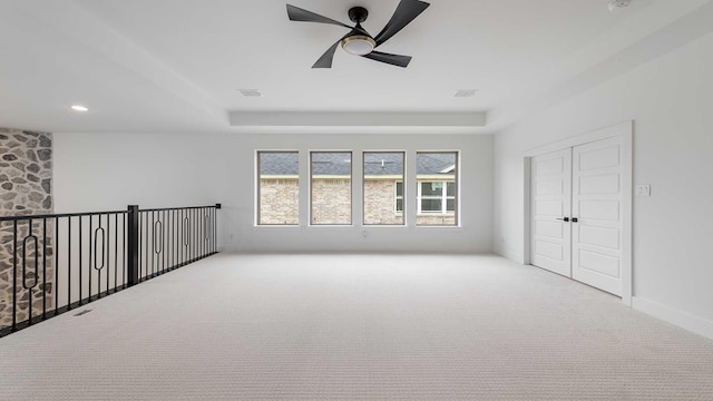 empty room featuring visible vents, a raised ceiling, carpet floors, and a ceiling fan