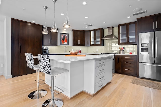 kitchen featuring a center island, wall chimney exhaust hood, light hardwood / wood-style flooring, backsplash, and appliances with stainless steel finishes