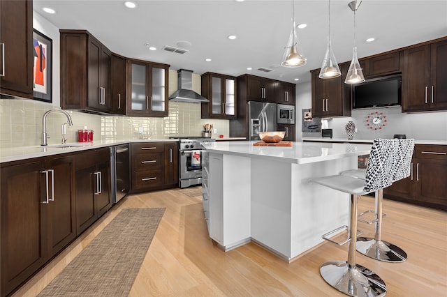 kitchen with stainless steel appliances, light hardwood / wood-style floors, sink, wall chimney exhaust hood, and a center island