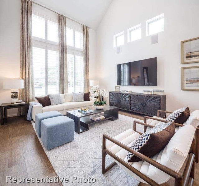 living room featuring high vaulted ceiling, a fireplace, wood-type flooring, and a healthy amount of sunlight